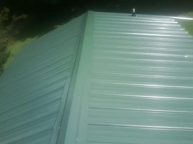 New green metal panels meeting at the ridge of a roof — Flat Roof Repair work by our crew in Saint Cloud
