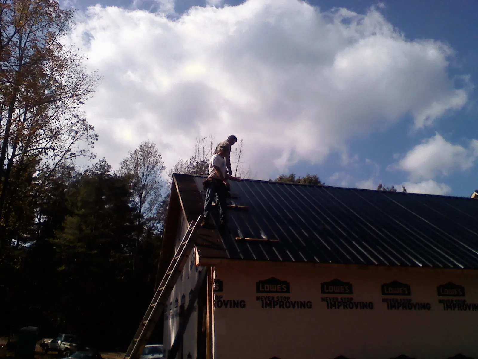 Roofer fastening dark metal panels high against a cloudy sky, from a Roof Inspection job in Saint Cloud