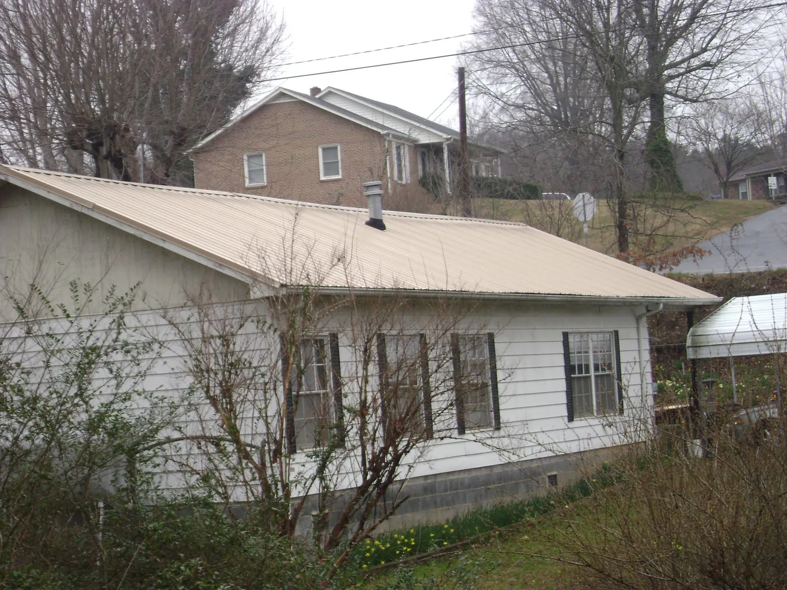 Tan metal roof on a white sided house set into a hillside — Commercial Roofing by Roofing Brothers in Saint Cloud