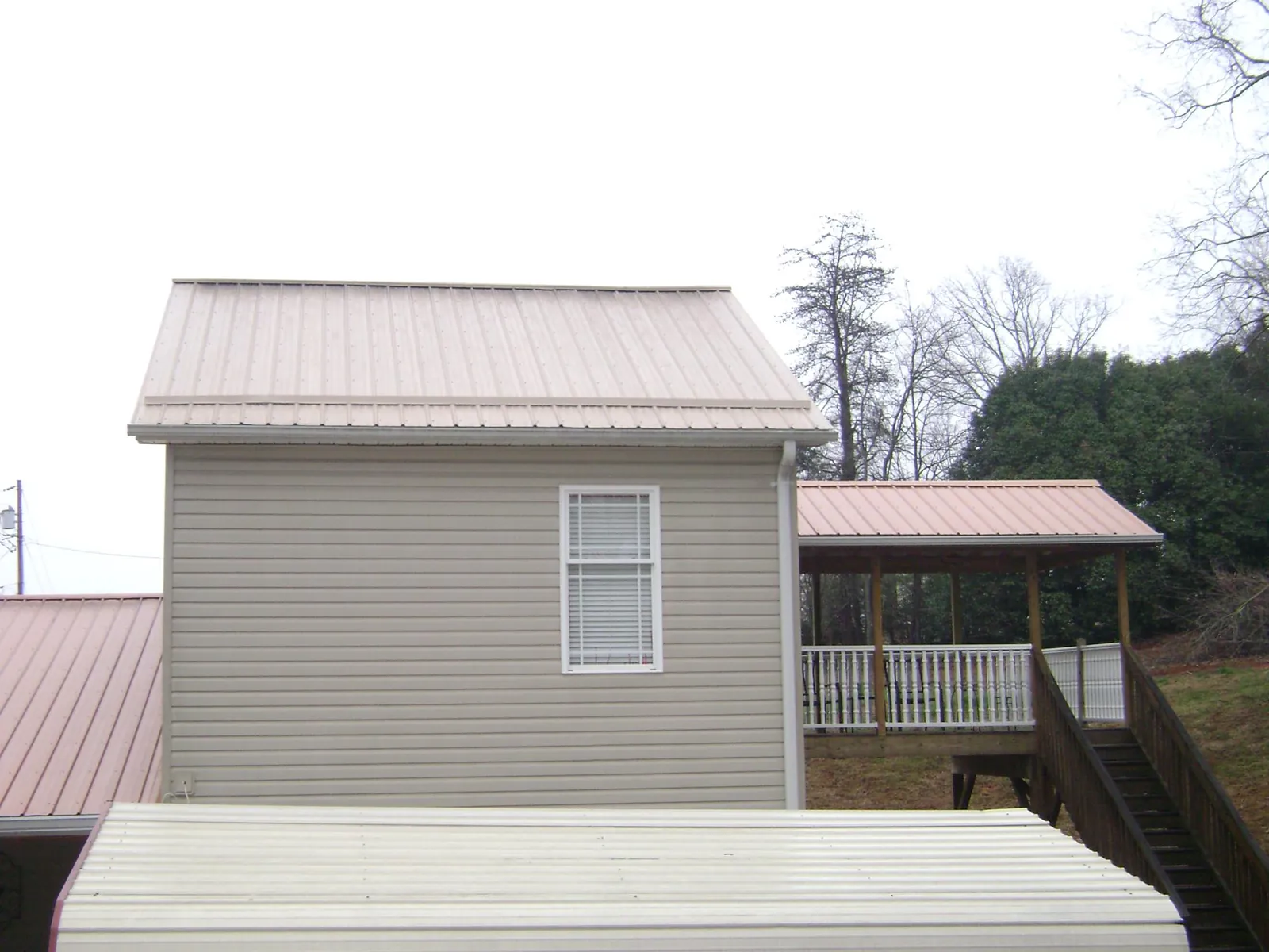 Tan metal roofs on a two story addition and attached porch, from a Roof Replacement job in Saint Cloud